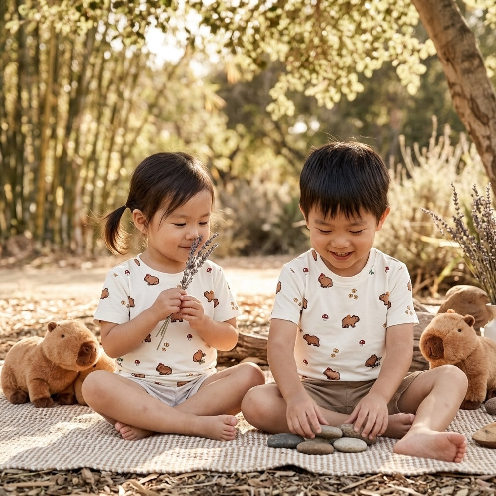 2 kids sitting below tree wearing Cuteboid bamboo t shirt with capybaras prints. Cooling and breathable materials that is suitable for outdoor activities